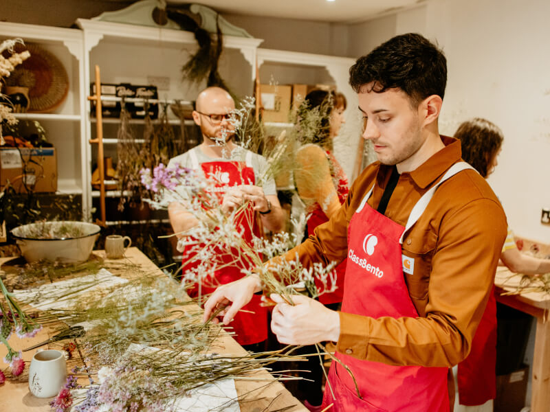 Young man in an apron holding stems of dried flowers in a florist